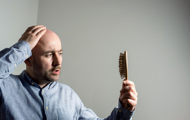 Confused bald man with hair brush