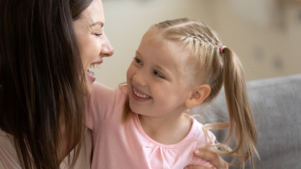 Close up of cute little girl child hug smiling young mom make peace or reconcile, happy small preschooler daughter embrace cuddle with excited mother or nanny have fun together showing love and care