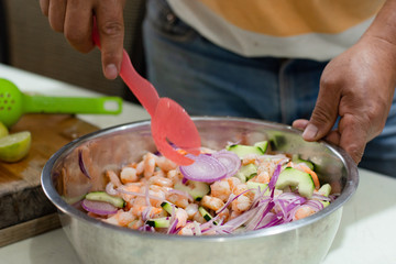 Mexican seafood made with shrimps and vegetables in a bowl is being prepared by an unrecognizable person