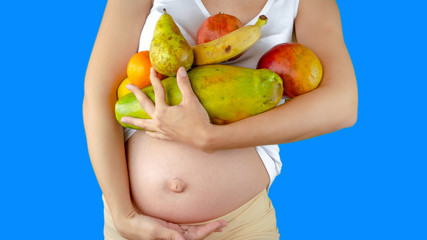 A happy pregnant young woman holding fruits and vegetables next to her belly showing a healthy pregnancy diet with vitamins and lifestyle for a good nutrition and weight loss during 9 months.
