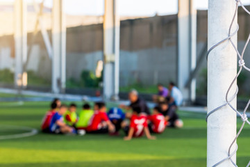 White mesh goal with blurry young boy soccer players sitting.