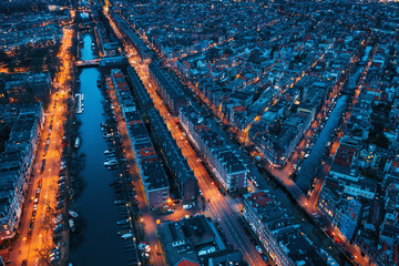 Beautiful night aerial view of Amsterdam downtown from above with many narrow canals, illuminated streets and old historic houses, drone photo. - obrazy, fototapety, plakaty