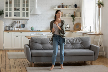 Obraz premium Overjoyed young woman enjoy free leisure weekend at home dancing listen to music in living room, smiling happy millennial female have fun moving to rhythm being active in modern studio home
