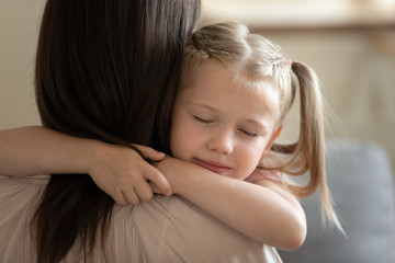 Close up of sweet small preschooler girl embrace young mother showing love and care enjoy...