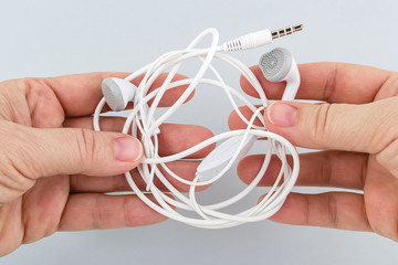 Female hands holding tangled earphones on a gray background. White tangled headphones. Modern...