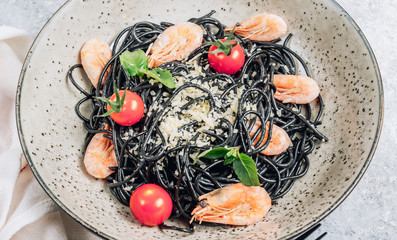 Fototapeta na wymiar Black pasta with seafood. Traditional Italian cuisine - pasta with shrimp, tomato and basil in a ceramic plate on a rustic background. Flat lay, top view.
