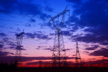 Fototapeta premium Many high voltage towers, silhouetted against the setting sun