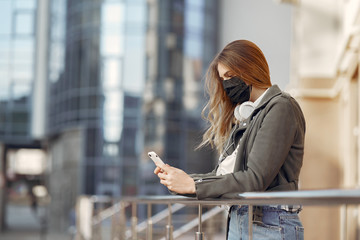 Woman in the city. Person in a mask. Coronavirus theme. Girl walks with phone and headphones.