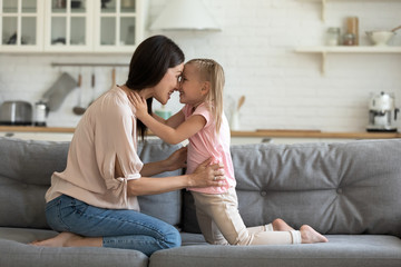 Naklejka na ściany i meble Happy little preschooler girl and young mother touch noses foreheads look in eyes enjoy tender sweet moment together, smiling loving mom and daughter have fun playing together at home on weekend