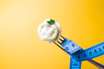 one dumpling with a leaf of parsley on a fork, a measured blue tape wrapped around the fork to measure waist and body volume, weight loss and diet concept