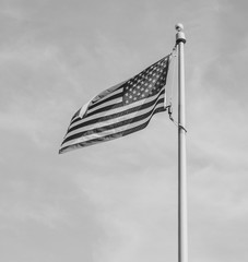 Close up black and white image of the American flag on a flag pole blowing in the wind against a grey sky