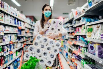 Toilette paper shortage.Woman with hygienic mask shopping for toilette paper supplies due to panic buying and product hoarding during virus epidemic outbreak.Hygiene products deficiency - obrazy, fototapety, plakaty