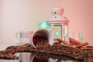 Still life in pastel colors. A Cup that spills coffee beans. A white Cup and a lantern with a candle. Turquoise and pink.