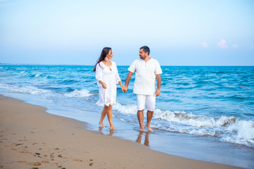 Fototapeta na wymiar Couple of lovers just married, honeymoon. Elegant and attractive happy family man and woman walking at sea coast. Young wife and husband in love