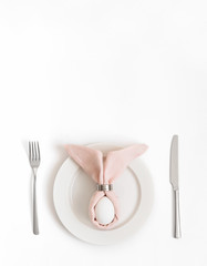 Easter table setting with egg in pink Easter bunny napkin on a white background. Vertical orientation.