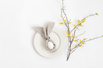 Easter table setting with egg in gray napkin Easter Bunny and a branch of yellow forsythia flowers on a white background.