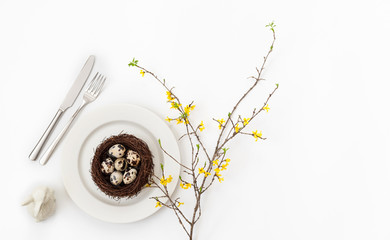 Easter table setting with quail eggs in a nest , a branch of yellow forsythia flower and a rabbit...