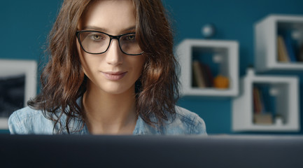 Portrait of young serene woman with loose curly hair wearing eyeglasses looking at computer screen