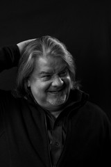 Studio head shot of man while he is laughing and touching his head. This is a monochrome image.