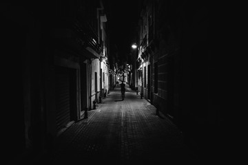 Woman walking alone in the street late at night.Narrow dark alley,unsafe female silhouette.Empty streets.Woman pedestrian alone.Police hour.Assault situation,violence against women concept. - Powered by Adobe