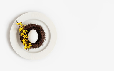 Easter beautiful table setting with a chicken egg in a nest and a yellow flower forsythia on a...