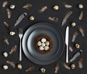 Easter dark table setting with a nest of quail eggs on a black background. Easter pattern.