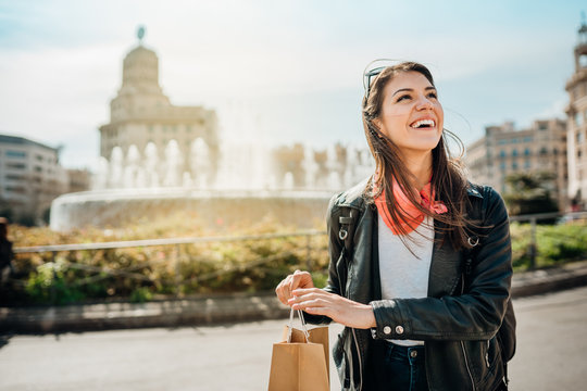 Cheerful young female tourist shopping on Catalonia Square(Placa de Catalunya),La Rambla street,Barcelona,Spain.Best shopping in city center.Tourist spring/fall shopping experience.