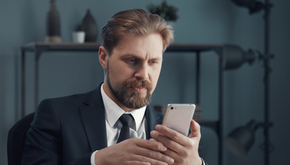 Obraz na płótnie Canvas Portrait of mature businessman in formal attire looking at smartphone screen sitting in office