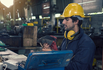  Technician in a mechanic's uniform wearing a yellow helmet, wearing headphones, resting and cleaning the equipment in the factory.