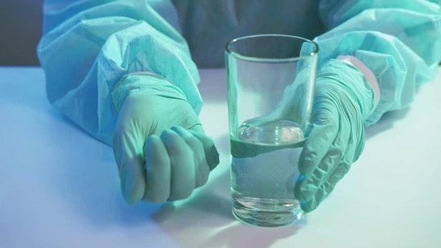 Coronavirus disease. Antibiotic therapy. Nurse hands in gloves offering drugs water glass.