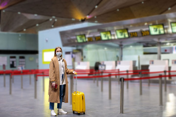Naklejka premium Woman with luggage stands at almost empty check-in counters at the airport terminal due to coronavirus pandemic/Covid-19 outbreak travel restrictions. Flight cancellation.Quarantine all over the world