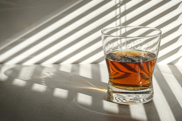 Whiskey or brandy in a glass near the window. Blinds and daylight.