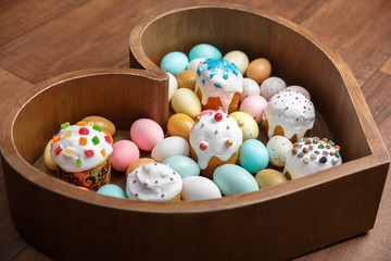 A lot of easter multi-colored eggs and cake in wooden box heart form on wooden background. Spring and Easter holidays. Minimalistic design. Horizontal frame. Close up