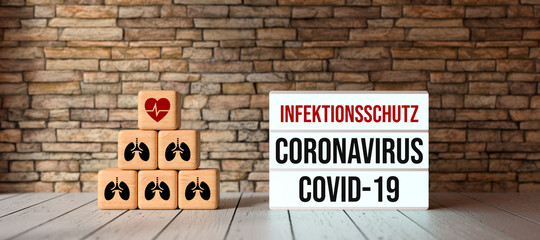 cubes with medical symbols and lightbox with text CORONAVIRUS COVID-19 and INFECTION PROTECTION in German in front of a brick wall