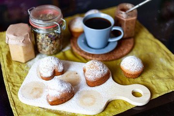 muffins with icing sugar on a table, among other kitchen utensils a cup of coffee