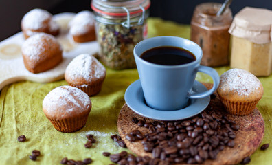 muffins with icing sugar on a table, among other kitchen utensils a cup of coffee
