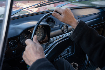 Naklejka premium Unrecognizable man holding hands on steering wheel and driving retro car through country road at sunny autumn day. Guy controlling his auto riding at highway on high speed