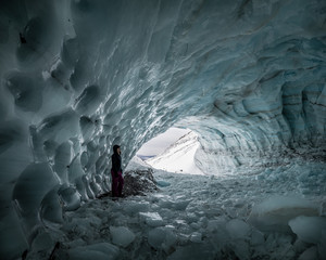 Hiking through an amazing ice cave in Yukon Territory, Canada. Winter in Yukon Territory. One person, hiker, woman in view and amazing smooth, ice formations walls.