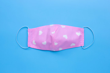 Handmade pink cloth with white heart mask on blue background.