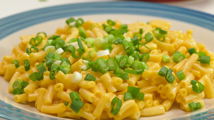 Macaroni and cheese with fresh chopped green onion close up on a plate on a kitchen table