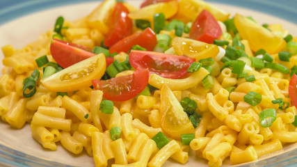 Macaroni and cheese with chopped green onion and sliced cherry tomatoes close up on a plate