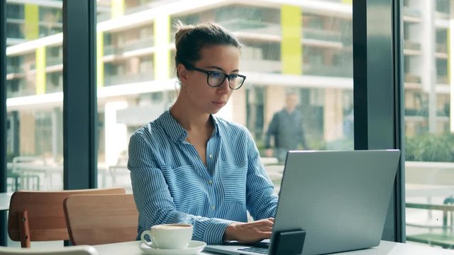 Gorgeous lady is operating a laptop while being in a cafe