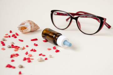 Still life : eye drops dark glass bottle, seashell and colored stones, natural medicine, red glasses