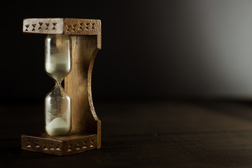 An old vintage hourglass sandglass with white sand on the wooden table. Black background, close up,...
