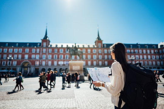 Visiting famous landmarks and places.Cheerful female traveler at famous Plaza Mayor square reading a map. Marid,Spain travel experience. Backpacker, travel photography.