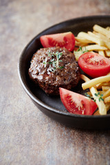 Hamburger steak with french fries and tomatoes. Brown stone background. Close up.	