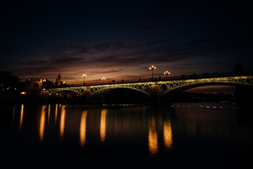 Obraz na płótnie Canvas Sunset over Guadalquivir river.Triana neighborhood with bridge of Isabel II. Beautiful sunset on the bank of Canal de Alfonso-XIII,Sevilla,Andalucia,Spain