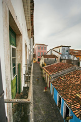Ladeira em Salvador, na Bahia. Casas antigas coloridas. Rua estreita vista de cima. Algumas pessoas andando.