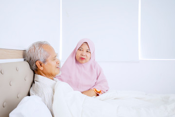Old muslim man resting on the bed with his wife