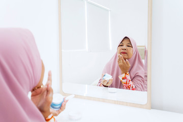 Old muslim woman applying skincare cream on face